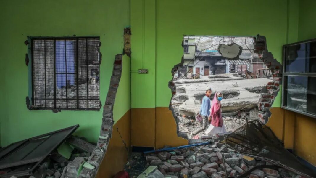 Seorang anak laki-laki dan perempuan Muslim berjalan melewati lubang di dinding sekolah yang dihancurkan di kota Haldwani, India utara, pada 9 Februari 2024, sehari setelah sekolah tersebut dihancurkan [Md Meharban/Al Jazeera]